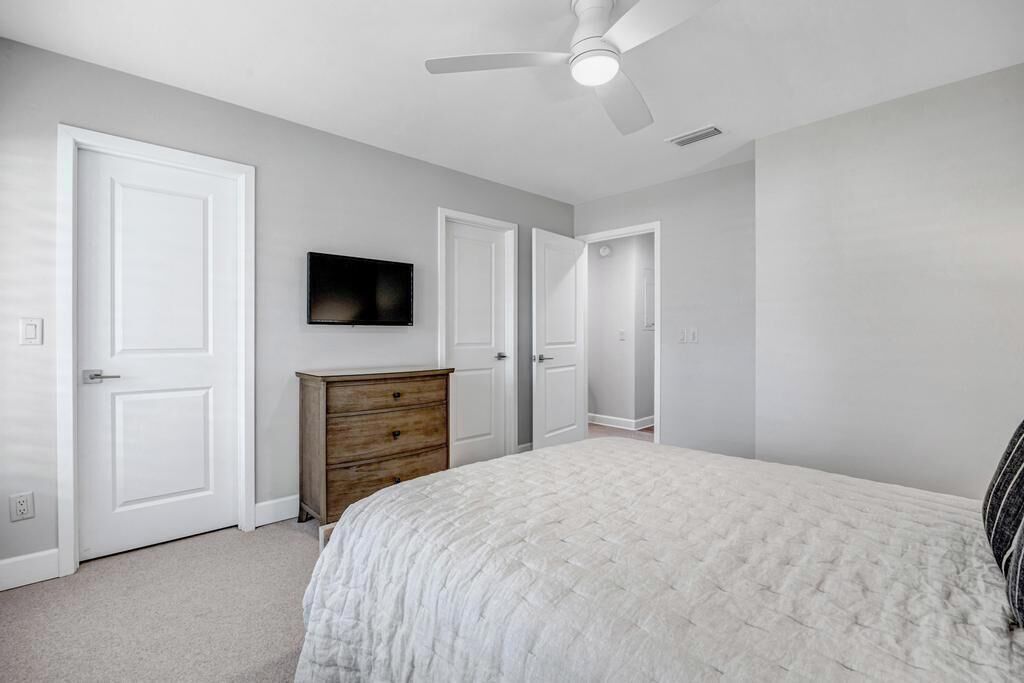A bedroom with a bed, a dresser, a ceiling fan, and a TV mounted on the wall.