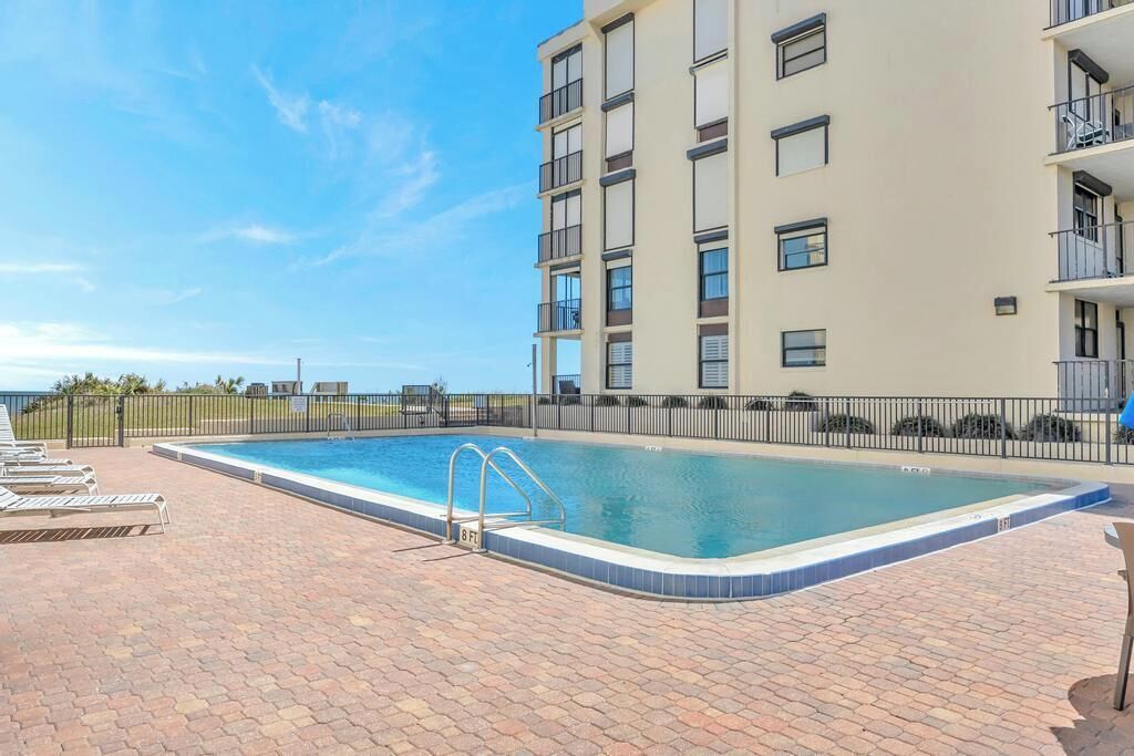 A swimming pool with a metal ladder, surrounded by a brick patio.