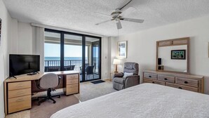 A hotel room with a bed, desk, chair, TV, and a balcony with a view of the ocean. - Crescent Breeze - Oceanfront w/incredible views, lanai & pool (St. Augustine)
