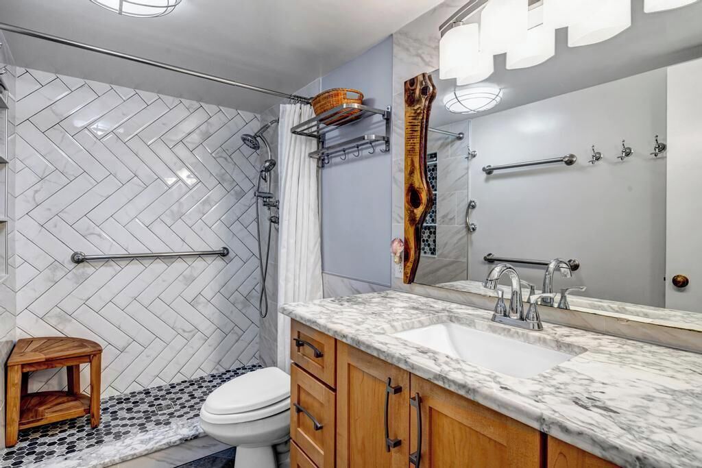 A modern bathroom with a herringbone tile wall, a wooden vanity, a large mirror, and a shower area.