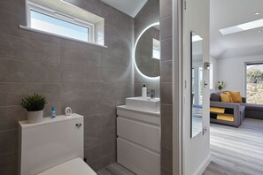 Een moderne badkamer met grijze tegels, een wit wastafel en een ronde spiegel.