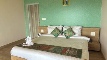Un letto rifatto con una coperta e cuscini a fantasia, un comodino in legno con una lampada, e una parete verde con una texture materica.