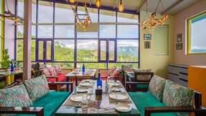 Un comedor con una mesa dispuesta para cuatro personas, amplias ventanas que ofrecen vistas al campo, y lámparas colgantes.