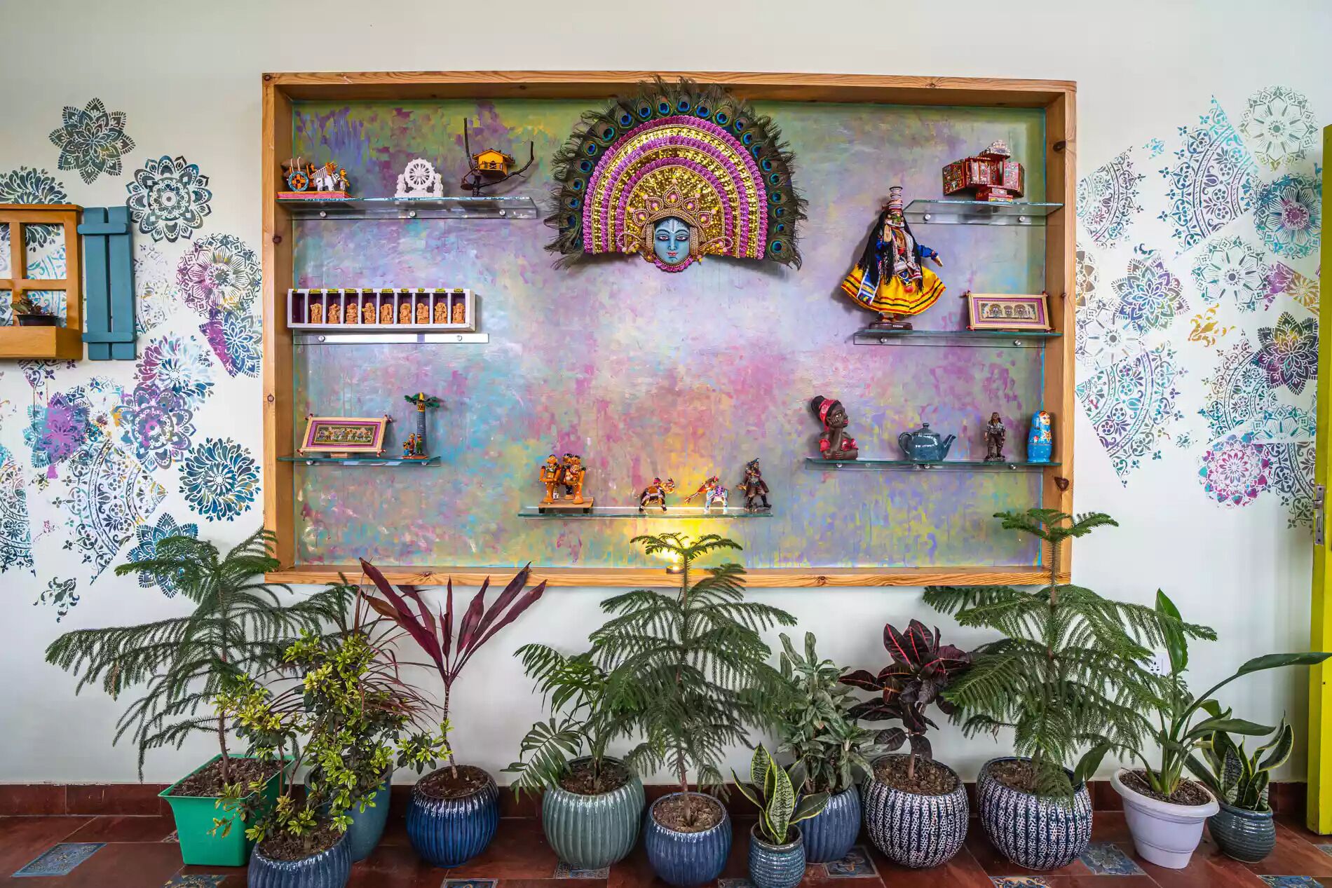 A wall with a colorful mandala design, shelves with decorative items, and potted plants.
