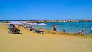Una playa con tumbonas y sombrillas, costa rocosa y gente nadando y relajándose.