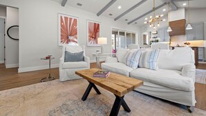 Una sala de estar moderna con una mesa de centro de madera, sofás blancos y una cocina al fondo.