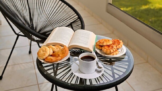 Een balkon met een tafel gedekt voor een maaltijd, een boek en een kop koffie.
