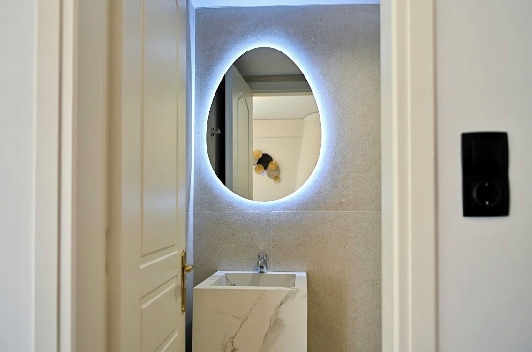 A bathroom with a marble sink, a circular mirror with underglow lighting, and a visible door.