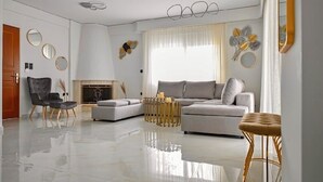 Een moderne woonkamer met een grijze bank, een zwarte fauteuil, een ronde salontafel en een open haard.