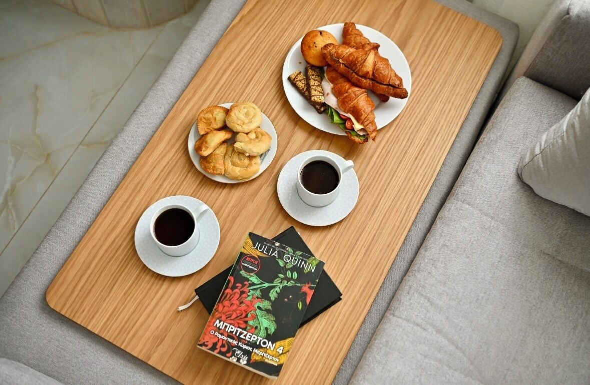 A wooden tray with croissants, a sandwich, and pastries on a table, accompanied by two cups of coffee and a book titled "Julia Quinn".