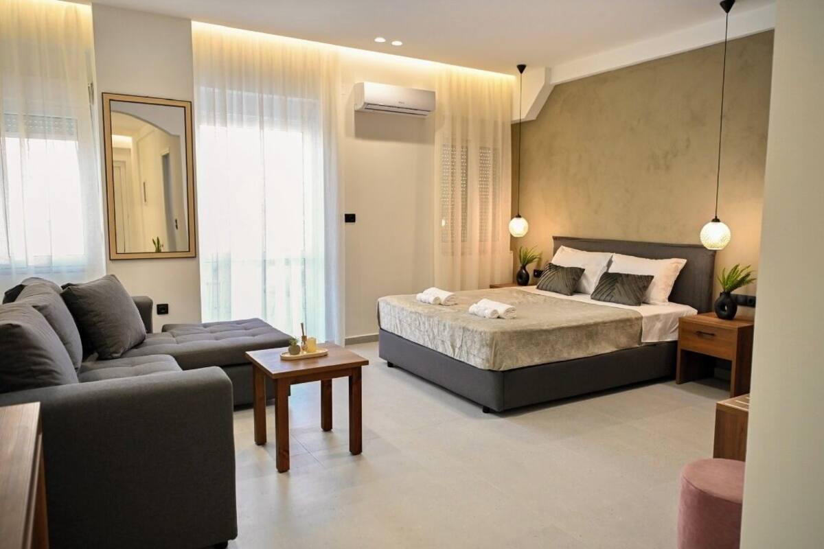 Un dormitorio moderno con una cama grande, un sofá, una mesita y una mesita de noche con lámpara.