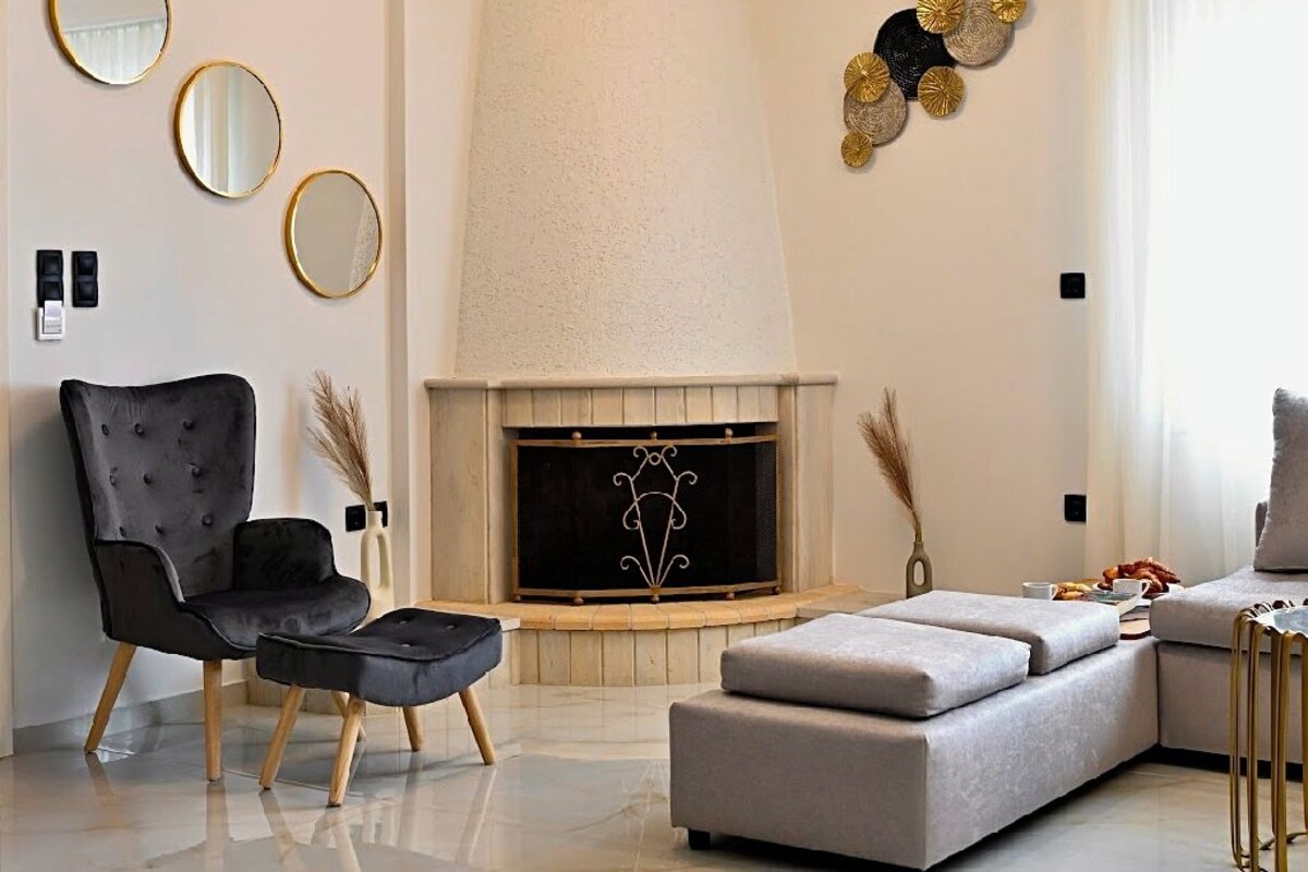 Een moderne woonkamer met een open haard, een zwarte fauteuil, een grijze bank en een decoratief wandobject.