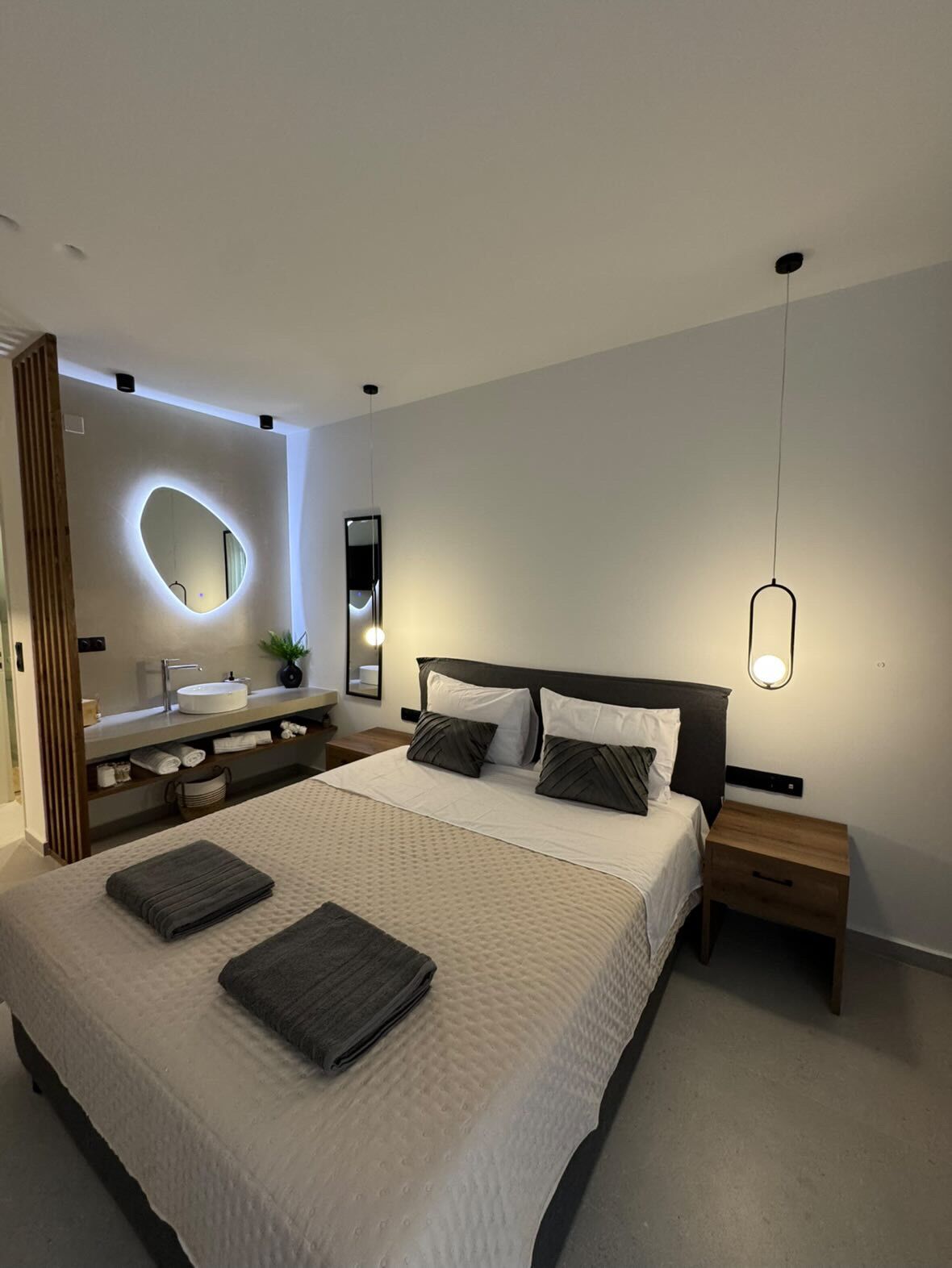 A modern bedroom with a large bed, bedside tables, a vanity with a mirror, and a hanging light fixture.