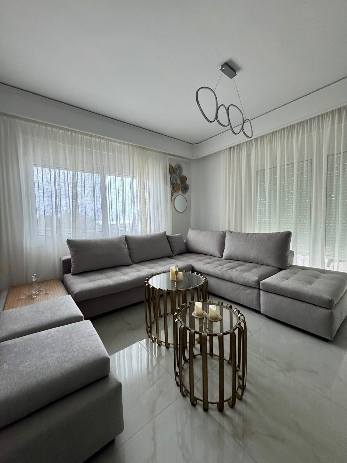 Una sala moderna con un sofá seccional, una mesa de centro de vidrio y un elemento decorativo en la pared.