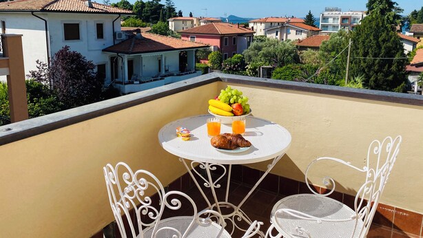 A balcony with a round table set for two, featuring a fruit bowl, croissants, and drinks.