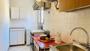 A compact kitchen with white cabinets, a red countertop, a stainless steel sink, and a window above the stove.