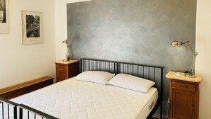 A neatly made bed with a quilted mattress, a large gray textured wall, and two bedside tables with lamps.