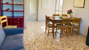 A dining area with a wooden table and chairs, a blue sofa, and a red bookshelf with decorative items.