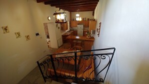 Eine Treppe führt zu einem Essbereich mit einem Holztisch und Stühlen, im Hintergrund befindet sich eine Küche und eine Wand mit Dekorationselementen.