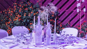 Ein Tisch, festlich gedeckt für einen formellen Anlass, mit klarem Glasgeschirr, Flaschen und einer Blumenarrangements.