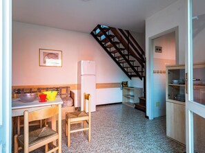 A kitchen with a wooden table, chairs, a refrigerator, and a staircase.