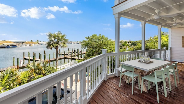 A wooden deck with a table and chairs, overlooking a marina with boats and a bridge in the background. - SEVENTH HEAVEN~Waterfront 5 BR, 4 Ba Townhome with Pool, Elevator & Dockage! (Key West)