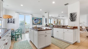 A spacious kitchen with white cabinets, a central island, and a dining area with a green chair. - SEVENTH HEAVEN~Waterfront 5 BR, 4 Ba Townhome with Pool, Elevator & Dockage! (Key West)