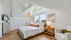 A bedroom with a bed, bedside tables, a TV, and artwork on the walls. - SEVENTH HEAVEN~Waterfront 5 BR, 4 Ba Townhome with Pool, Elevator & Dockage! (Key West)