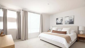 Une chambre spacieuse avec un grand lit, une table de chevet, un bureau et une fenêtre avec des rideaux.