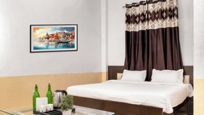 A hotel room with a bed, a glass coffee table, a framed painting, and a curtain with a pattern. - Hotel Sunrise Inn (Noida)