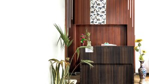 A reception desk with a dark wood finish, a patterned wall above, and potted plants on either side. - Hotel Sunrise Inn (Noida)