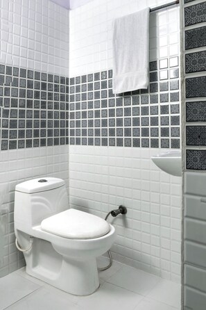 A bathroom with a white toilet and a mosaic tile wall, featuring a towel rack for guest comfort.