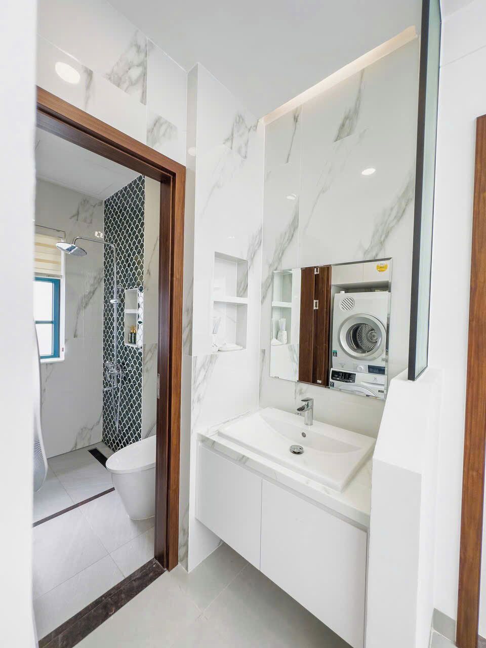 A modern bathroom with a built-in washing machine, a mirror, and a shower area.