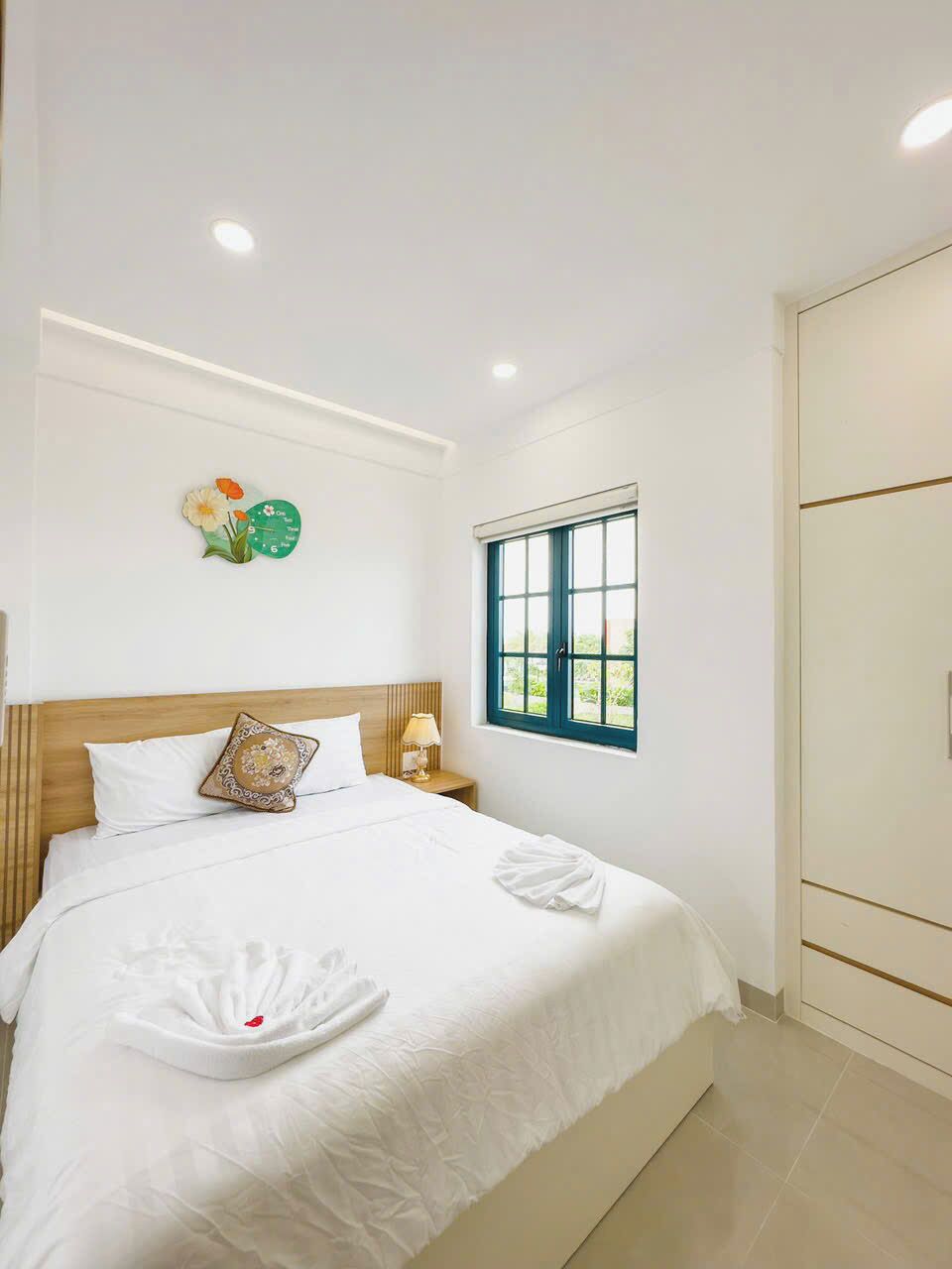 A hotel room with a bed, a window, a wardrobe, and a wall clock.