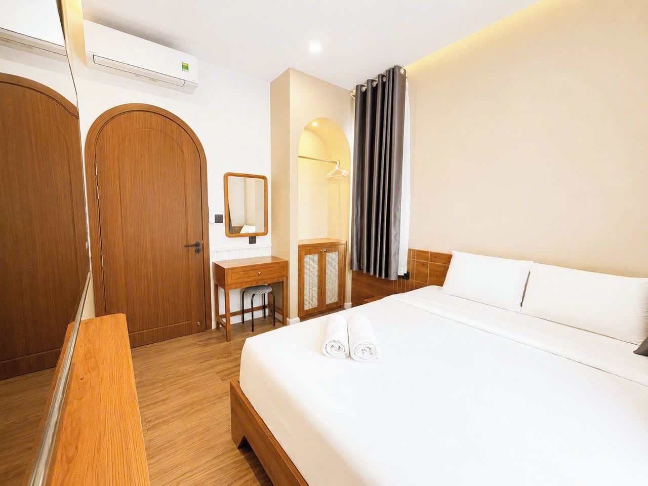 A hotel room with a bed, a desk, a chair, a wardrobe, and a mirror.