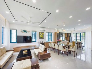 A spacious living room with a flat-screen TV, a sofa, a coffee table, and a dining area with chairs and a table. - Novaworld Phan Thiet - QT Villa (Tien Thanh)