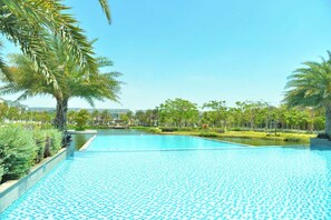 A large, clear swimming pool with a checkered pattern, surrounded by palm trees and greenery. - Novaworld Phan Thiet - QT Villa (Phan Thiet)