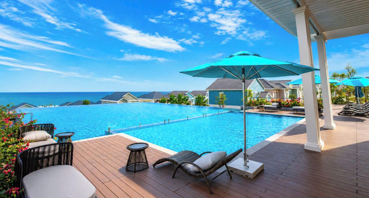 A pool area with lounge chairs and umbrellas, overlooking a clear blue ocean.