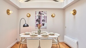 A dining area with a table set for four, a vase with flowers, and a painting of a building.