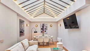 A modern living room with a high ceiling, a dining area, and a flat-screen TV mounted on the wall.