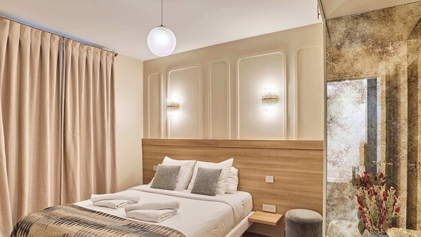 A modern bedroom with a wooden headboard, a large bed with white linens, a bedside table, a small stool, and a vase with flowers. - Superb air-conditioned flat on the Champs Elysées (Paris)
