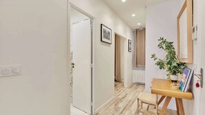A hallway with a wooden floor, a small wooden stool, a potted plant, and framed pictures on the wall. - Superb Apartment Invalides St Germain des Près (Paris)