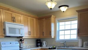 A kitchen with wooden cabinets, a white microwave, a stove, a coffee maker, and a bowl of fruit on the island. - Darnley Dream vacation home perfect to experience PEI to its fullest. (Kensington)