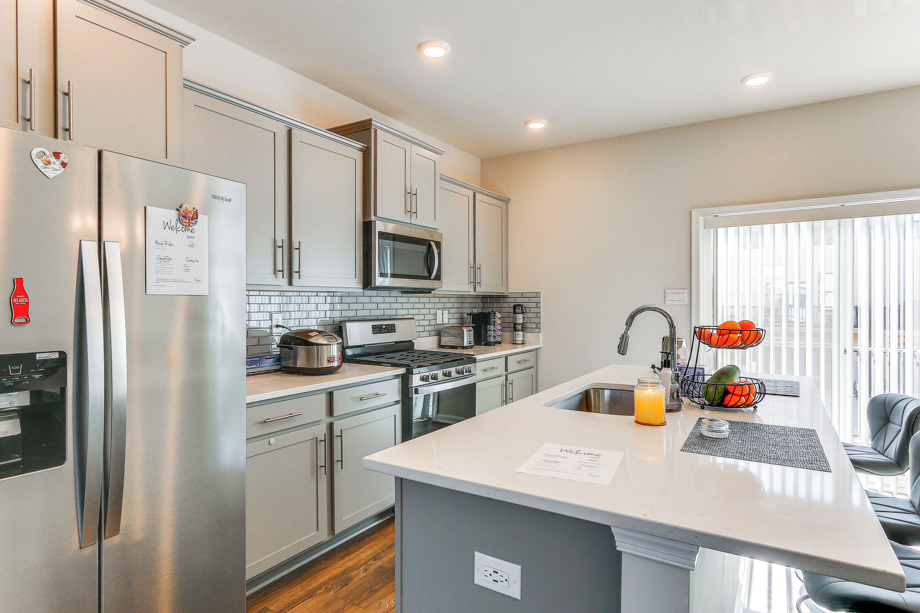 A modern kitchen with stainless steel appliances, a central island, and a view of the outside.