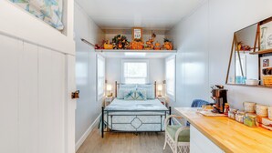 A bedroom with a bed, a nightstand, a chair, a window, and a shelf with decorative items.