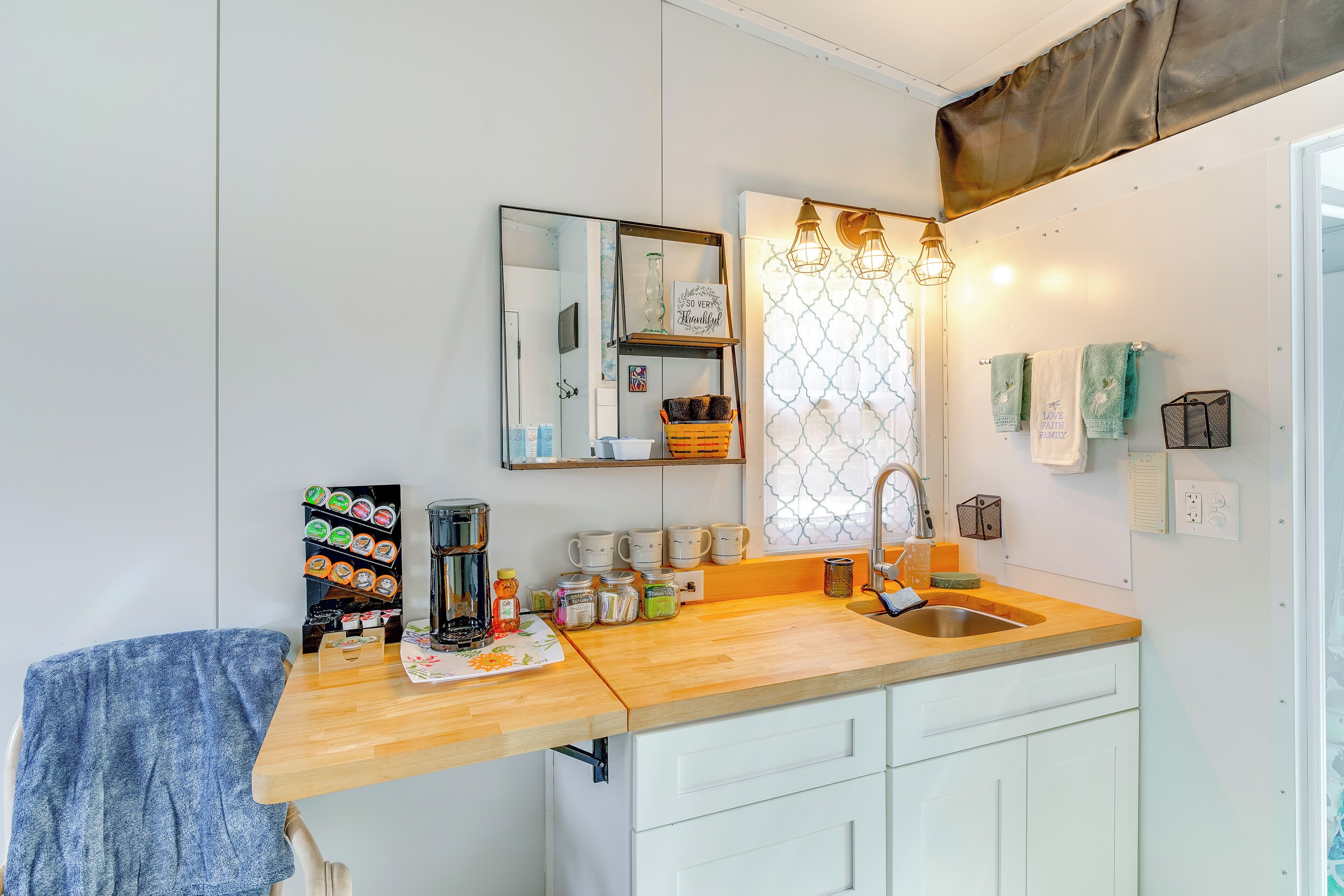 A modern kitchen with a wooden countertop, white cabinets, a large mirror, and a window with a decorative grid.