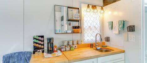 A modern kitchen with a wooden countertop, white cabinets, a large mirror, and a window with a decorative grid.