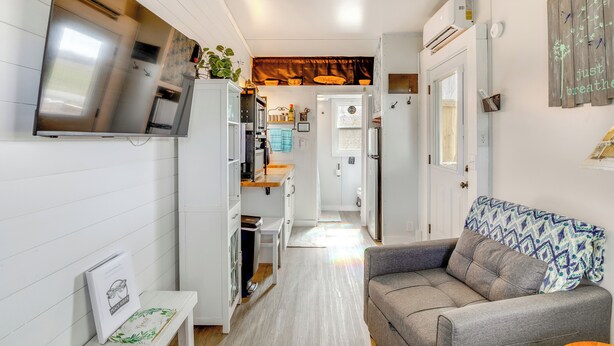 A compact living space with a kitchenette, a grey sofa, and a TV mounted on the wall.