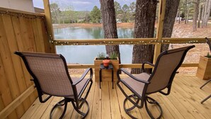 A wooden deck with two rocking chairs facing a lake, a small table with a potted plant, and string lights.