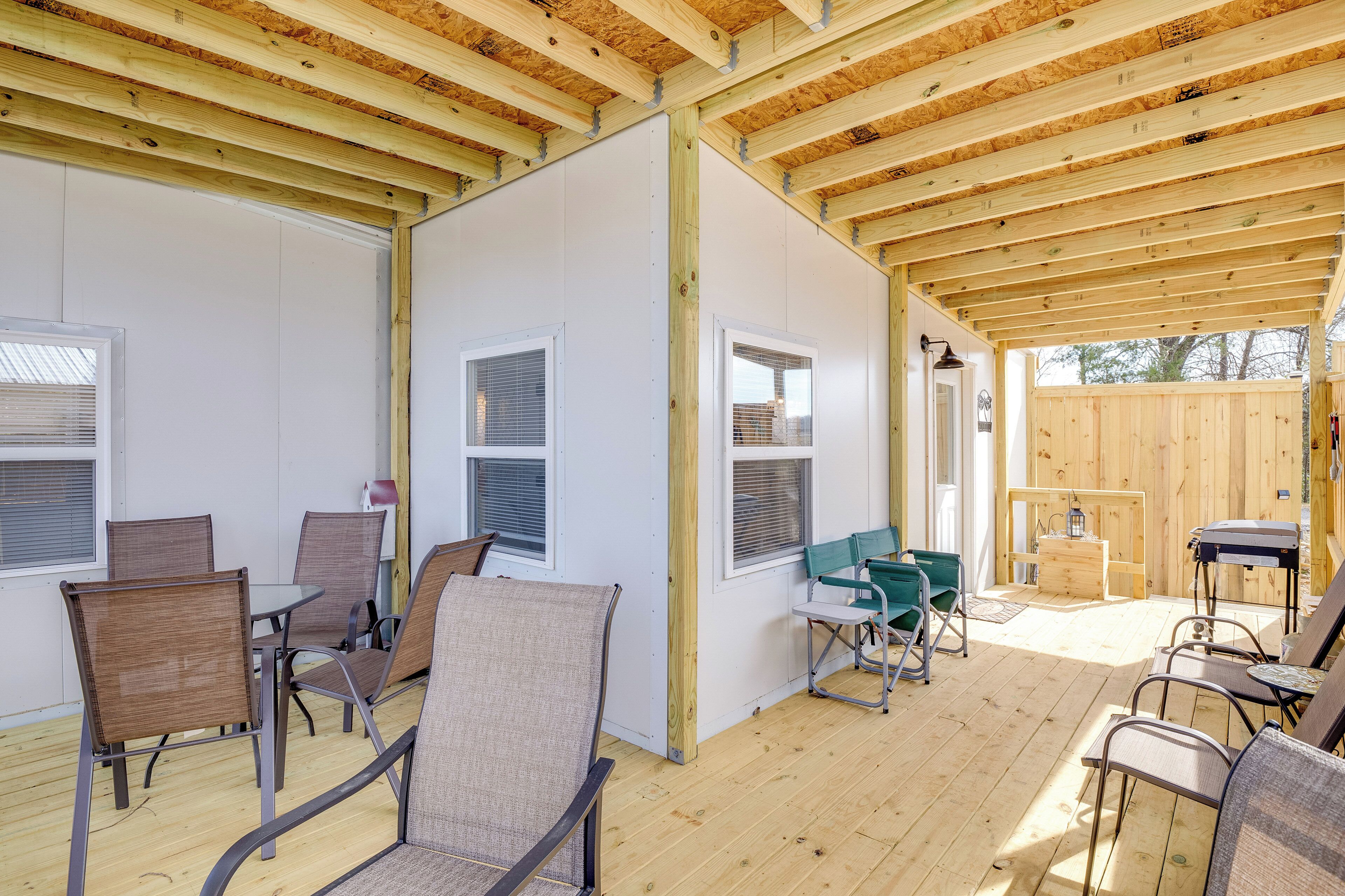 Un patio techado al aire libre con piso de madera, sillas de metal y una mesa.